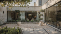 Showcase · Two clipped laurel cloud trees in stone pots on a gravel courtyard, framing a glazed garden room.