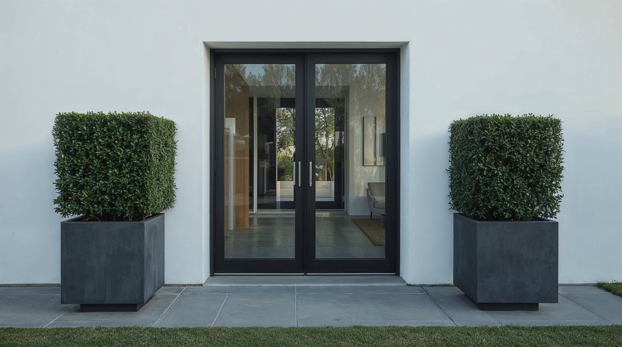 Pair of square yew (Taxus) cube topiary plants in large dark planters, symmetrically placed beside a modern black-framed glass entrance set into a white minimalist facade.